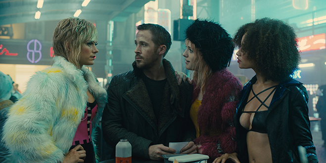 RYAN GOSLING as K and MACKENZIE DAVIS as Mariette in a street scene.