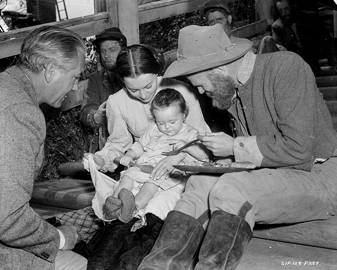 Behind-the-scenes with de Havilland and Ric Holt as Beau Wilkes (11 months) seated on her lap. Alongside her are director Victor Fleming and Phillip Trent as a hungry solider.