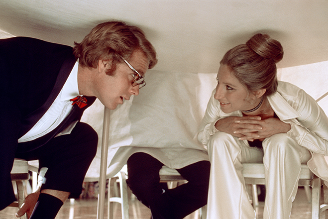 Ryan O'Neal as Howard Bannister and Barbra Streisand as Judy Maxwell crouched under table.